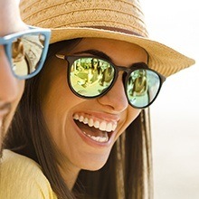 Smiling woman with glasses and sun hat after dental bonding