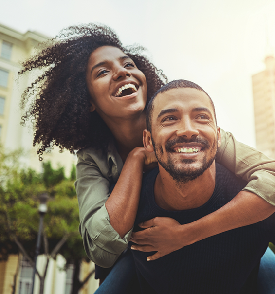 Smiling woman hugging a smiling man from behind after cosmetic dentistry in West Palm Beach