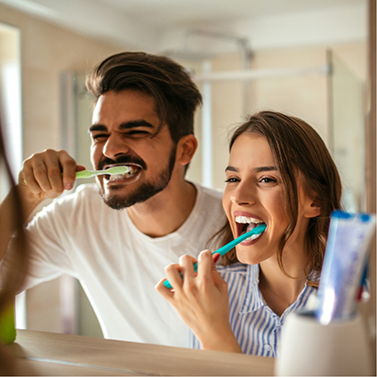 Man and woman brushing their teeth together in front of bathroom mirror