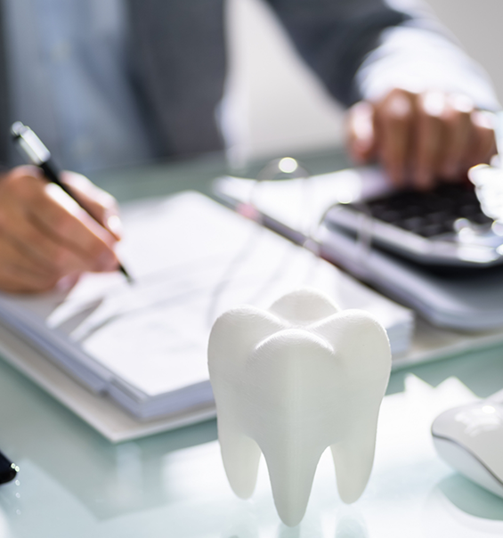 Person filling out paperwork on a desk next to a model of a tooth