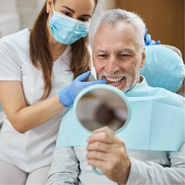 Man in dental chair looking at his smile in a mirror