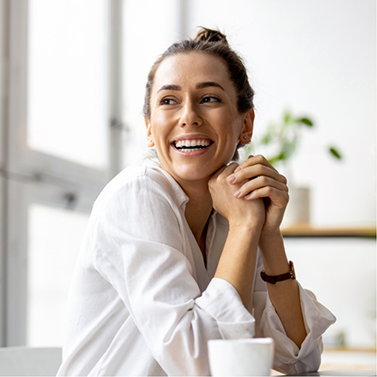 Smiling woman in white buttoned blouse sitting at kitchen table