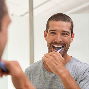 Man smiling while brushing his teeth