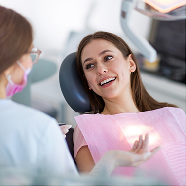 Woman leaning back in dental chair and smiling at her dentist