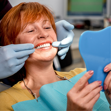 Dental patient with red hair admiring her smile in mirror