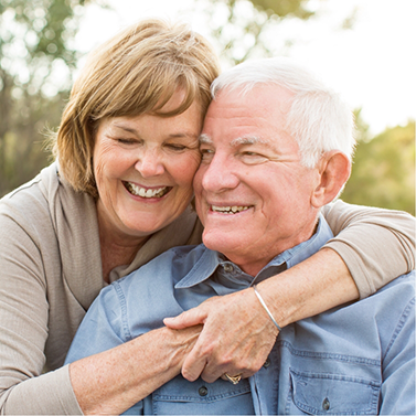 Senior man and woman grinning and hugging outdoors