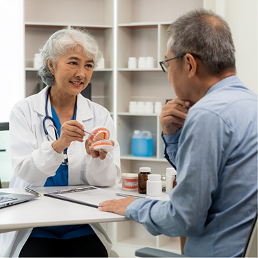 Dentist sitting across from a patient and showing him a model of a denture