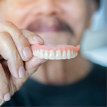 Man holding a denture in front of his face