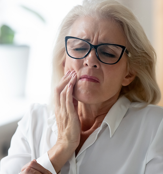 Woman wincing and holding her cheek in pain needing emergency dentist in West Palm Beach