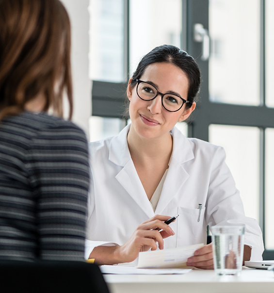 Woman in white lab coat sitting across table from someone