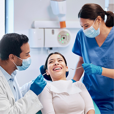 Woman in dental chair smiling with dentist and assistant