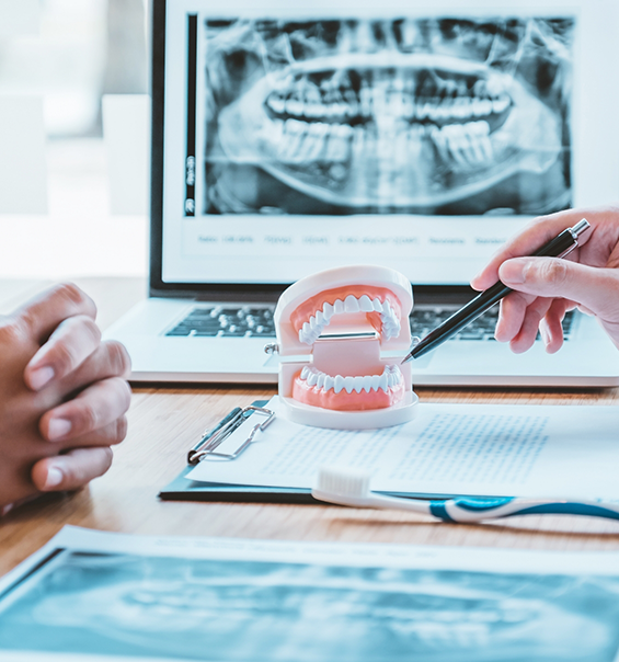 Dental patient sitting across from dentist at desk with computer showing x rays of teeth