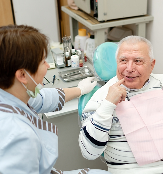 Senior man in dental chair pointing to his smile