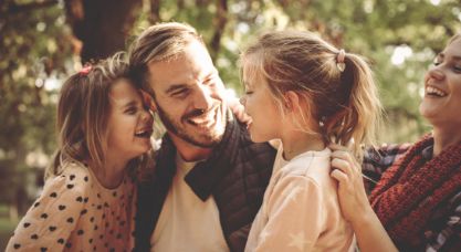 Man and woman laughing with their two young daughters outdoors