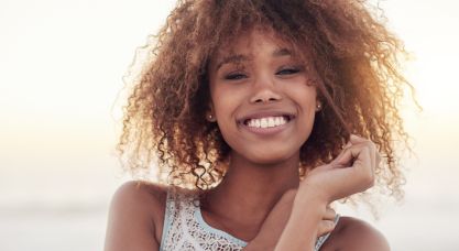 Young woman in white tank top grinning outdoors