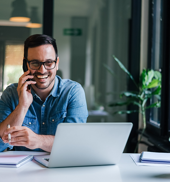 Man talking on phone while sitting at desk with laptop