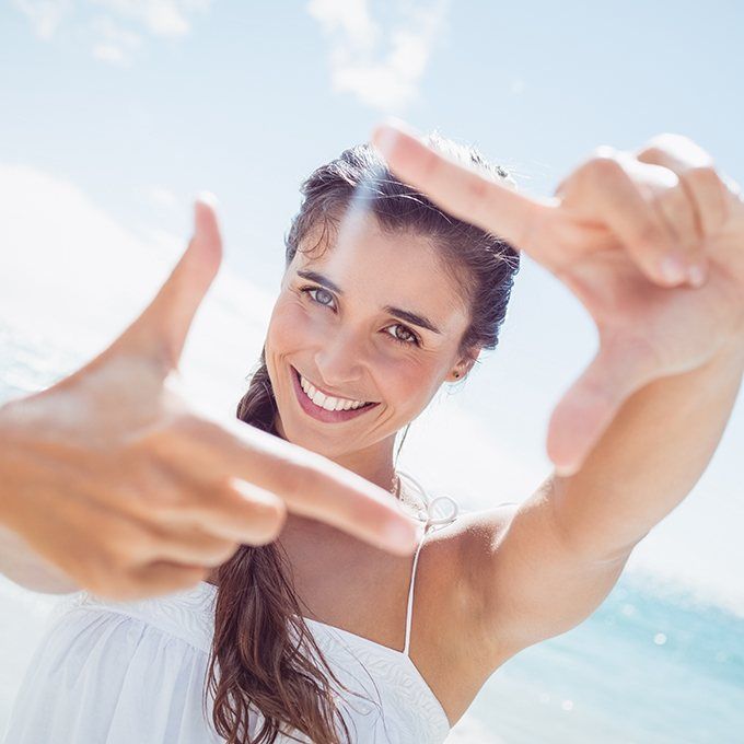 Smiling woman at beach after Invisalign treatment making photo frame with hands