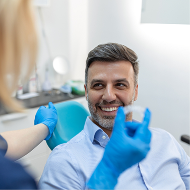 Dentist holding a clear aligner in front of a patient