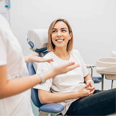 Woman in dental chair smiling while listening to her dentist talk