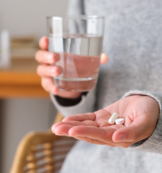 Person holding two pills and a glass of water