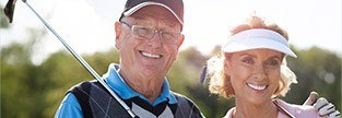 Two older patients smiling on golf course after restorative dentistry