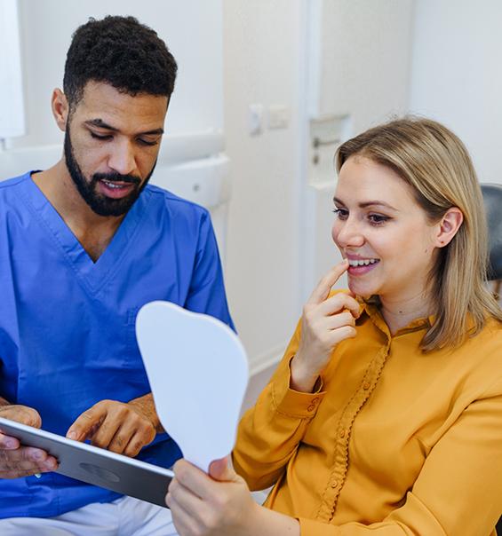 Woman in dental chair looking at her smile in a mirror