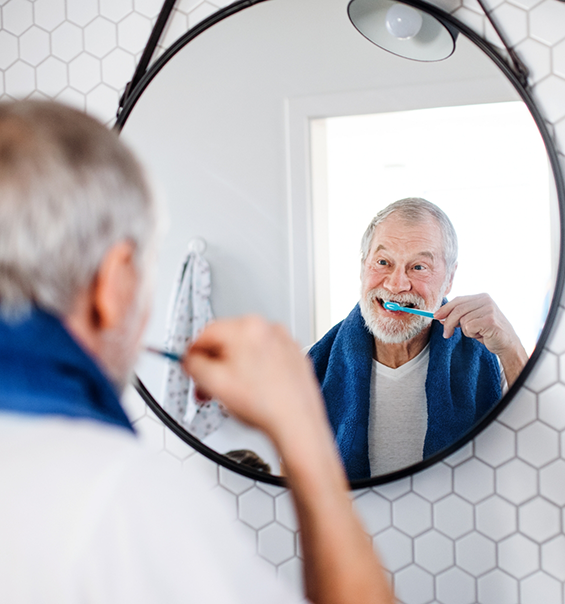 Senior man looking in mirror while brushing his teeth