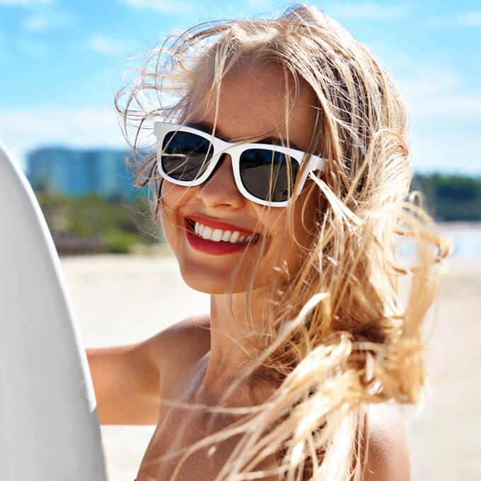 Young woman at beach holding surf board after teeth whitening