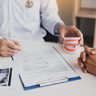 Dentist writing on clipboard at desk with model of dentures