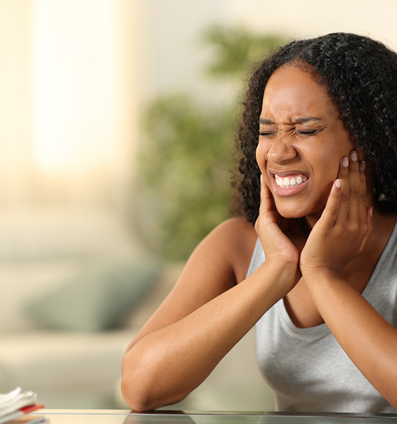 Woman wincing and holding her jaws in pain needing tooth extractions in West Palm Beach