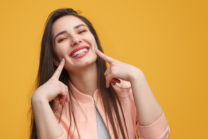 Woman on yellow background pointing to her smile